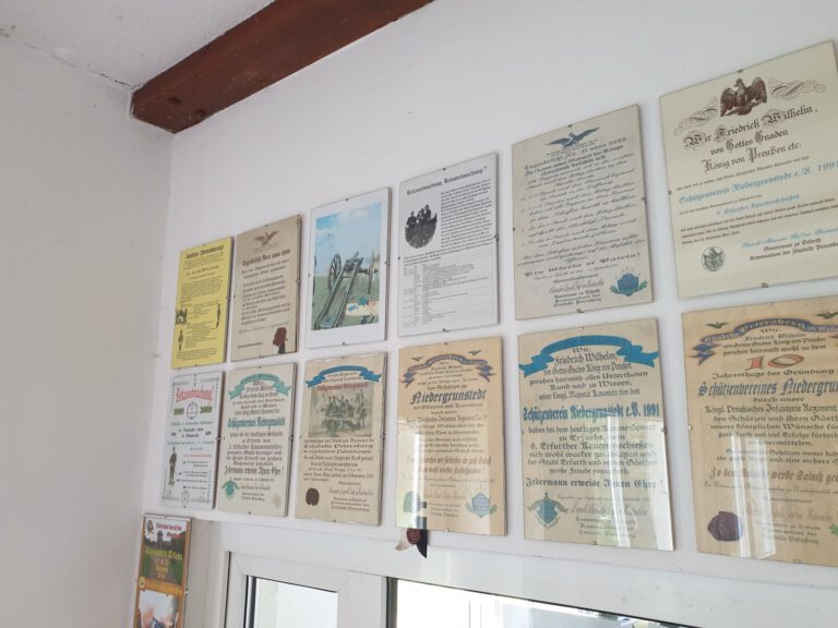 Eine Wand im Vereinshaus, dicht behängt mit gerahmten Urkunden in der Schrift und dem Stil preußischer Bekanntmachungen. Sie erinnern an das Erfurter Kanonenschießen und an die Gründung des Schützenvereins Niedergrunstedt im Jahr 1991.